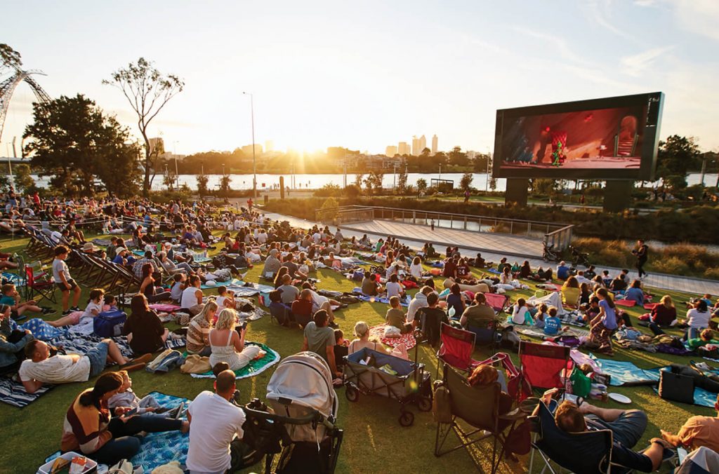 people watching a movie in a park on a large digital billboard